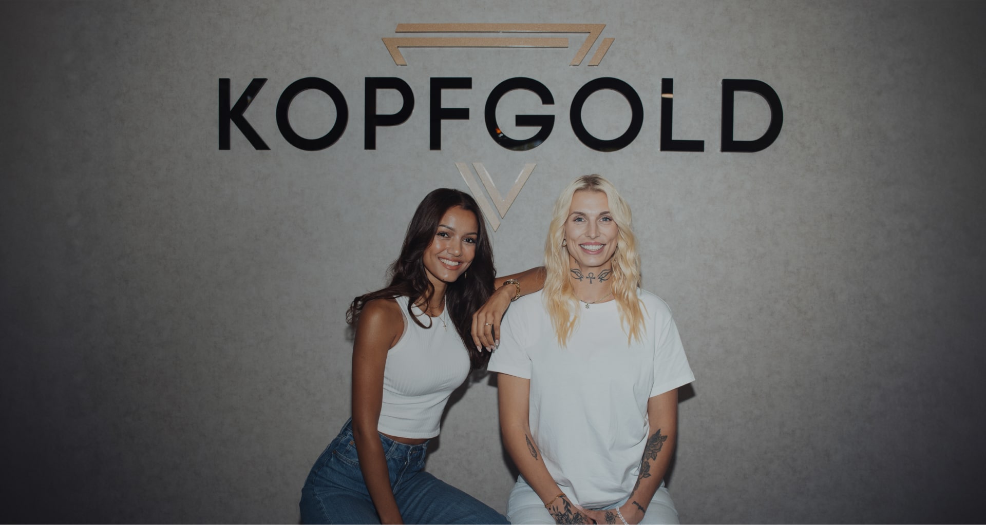 Zwei Frauen vor Wand mit Kopfgold Logo