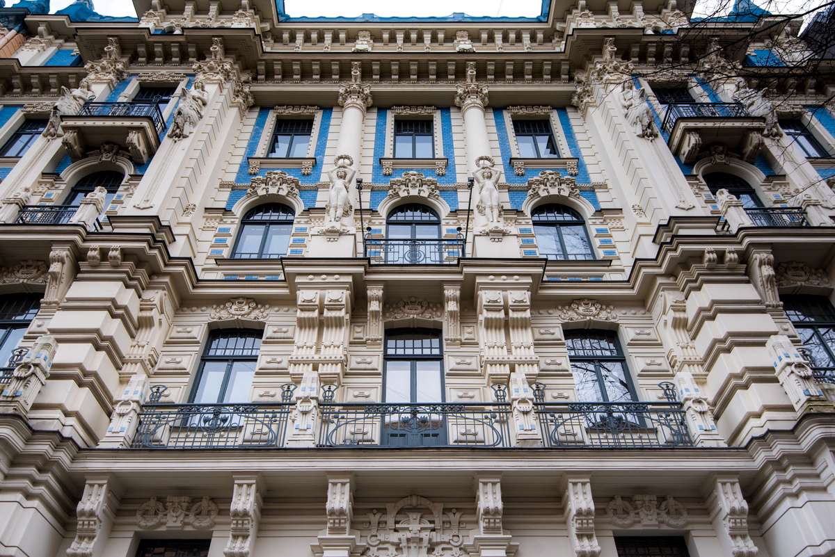 Ornate stone facade of a classical building with arched windows, decorative carvings, and blue-framed panes.