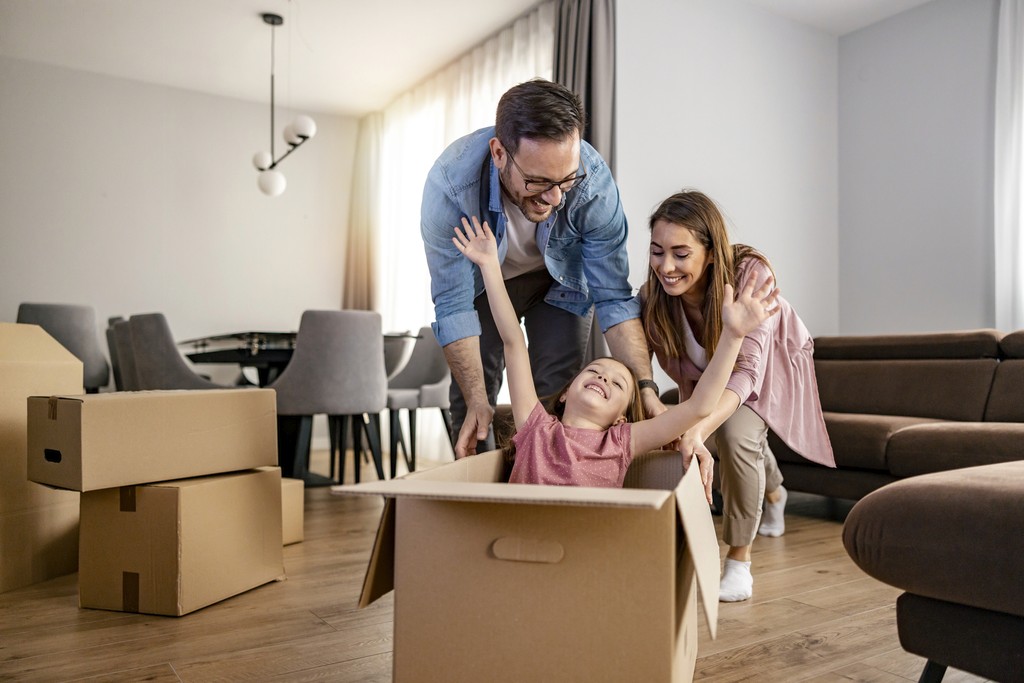 Srećna porodica u novom domu nakon selidbe – dete se igra u kutiji uz osmeh roditelja