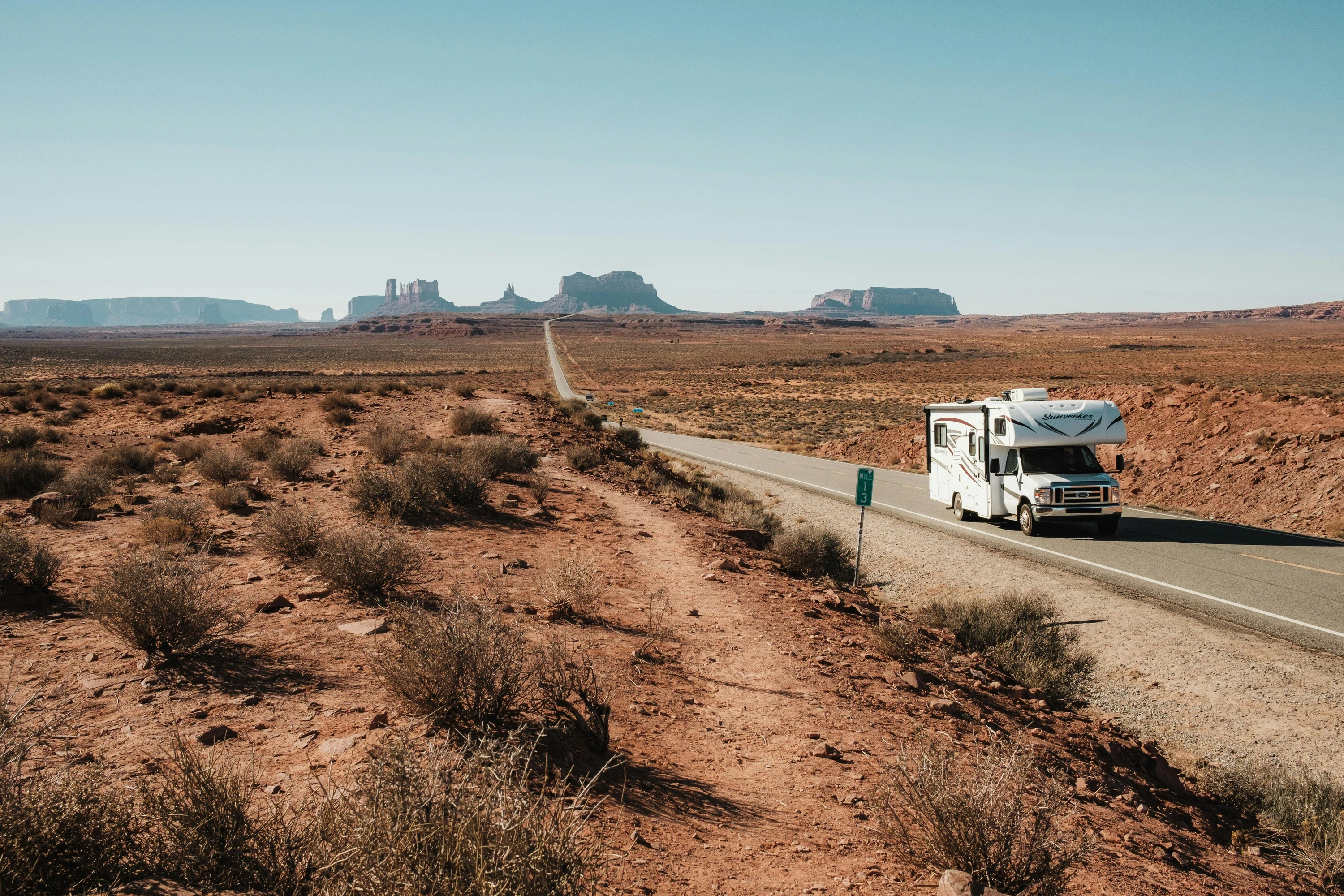 A white Sunseeker motorhome traveling on a long desert highway toward scenic red rock monuments.