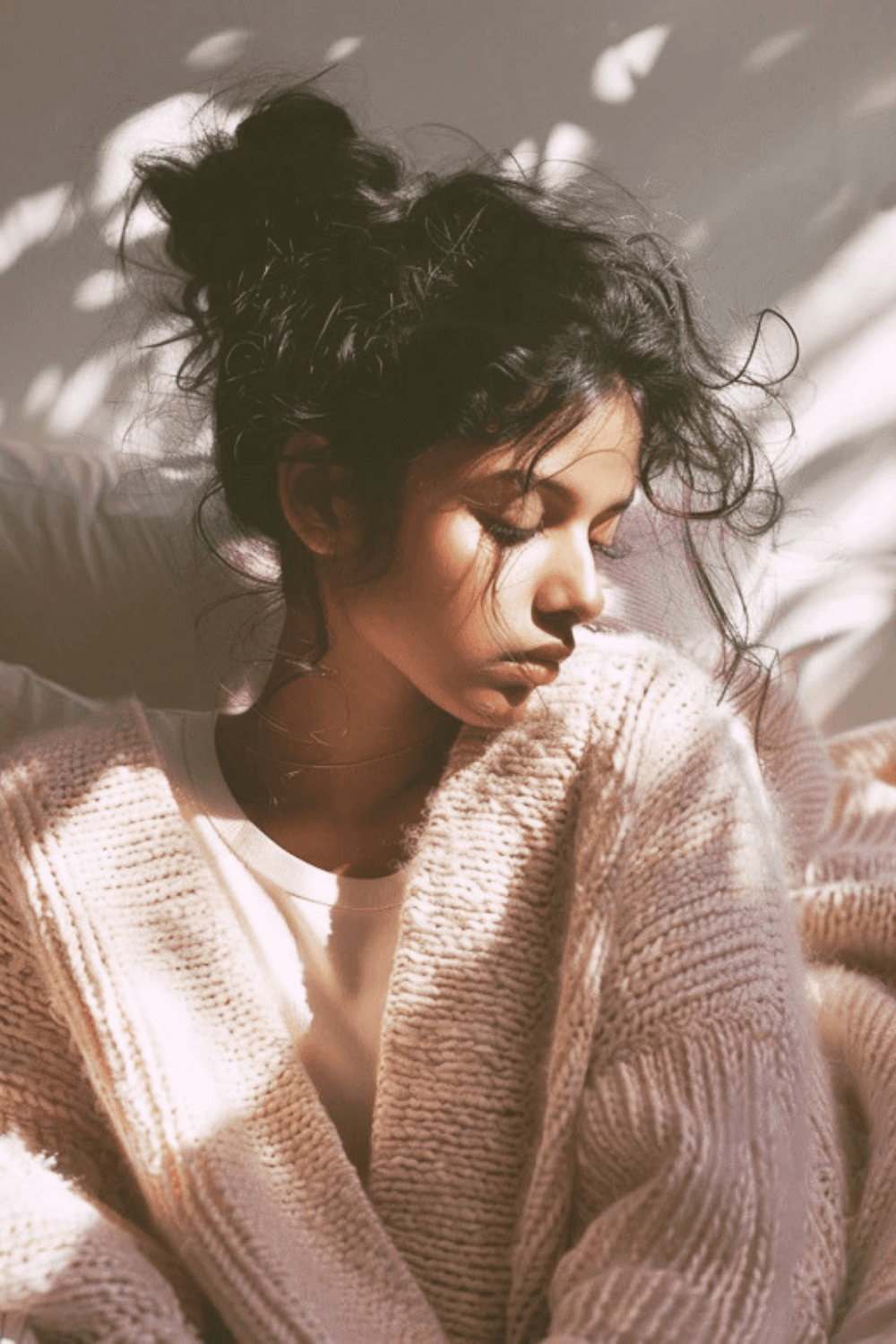 Postpartum mother sitting in soft light with eyes down, experiencing quiet physical discomfort and early recovery after childbirth