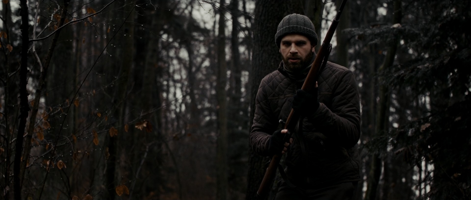 Exterior shot of a hunter aiming a rifle in a winter forest.