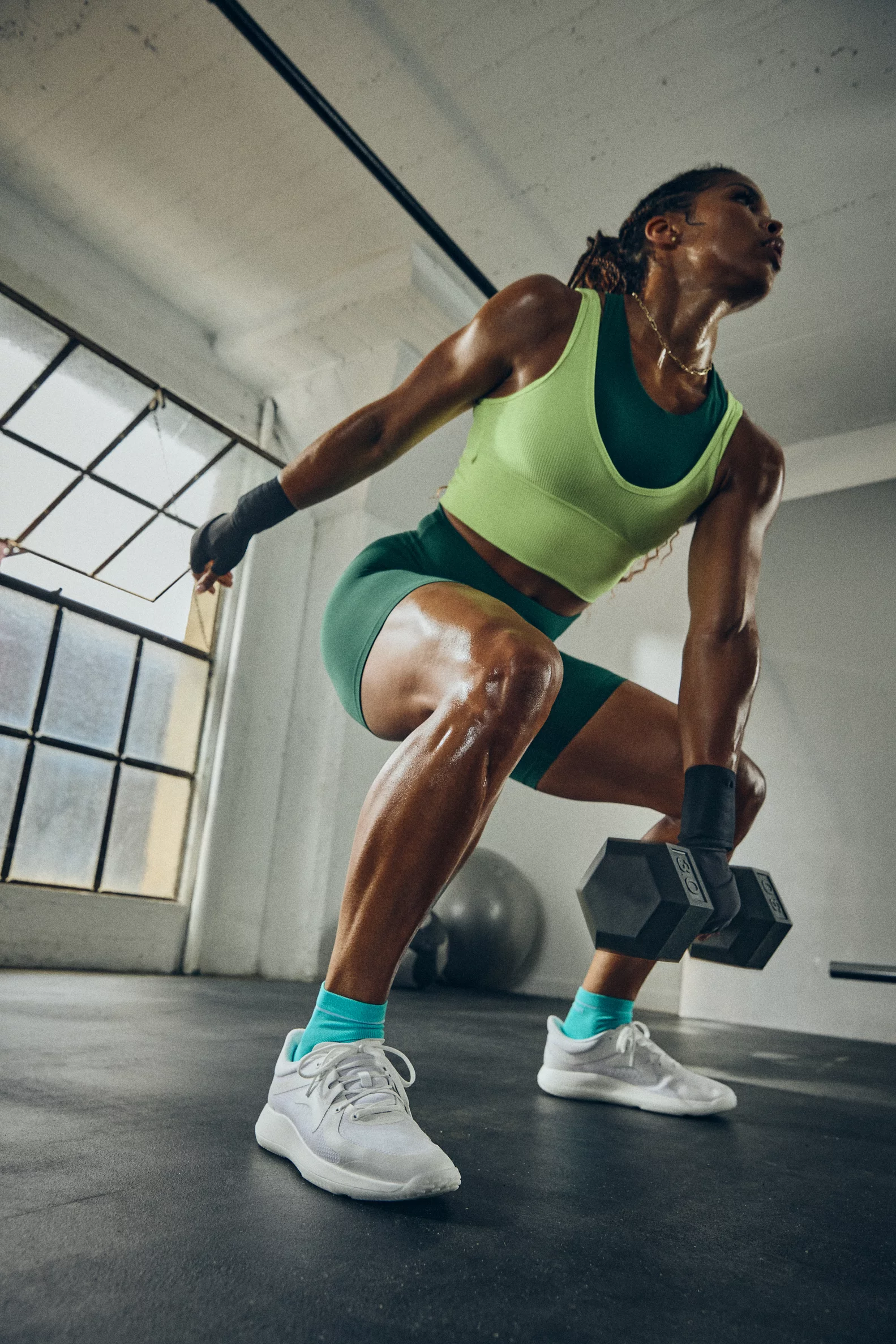 Sweaty, muscular woman doing a dumbbell squat in a gym.