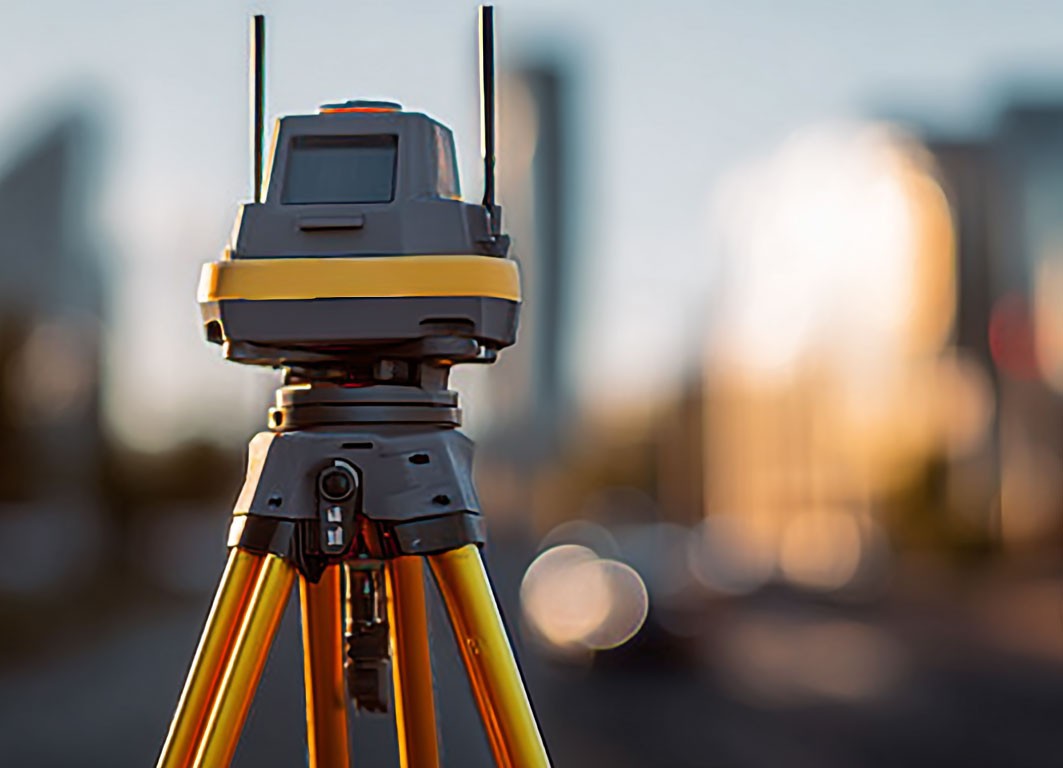 Surveying total station mounted on a tripod with a blurred city skyline in the background at sunset.