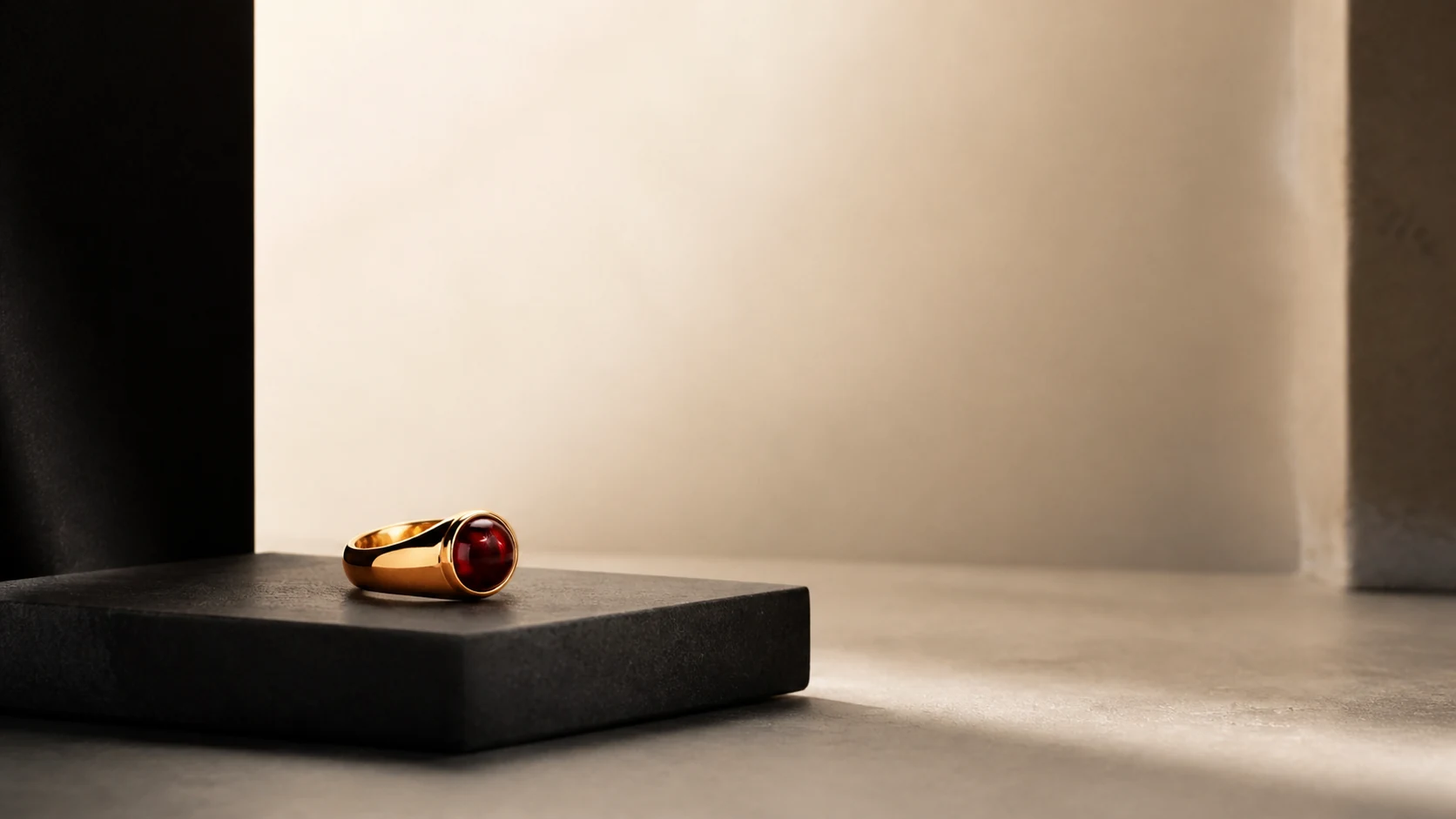 Gold ring with a deep red cabochon on a charcoal plinth under a long diffused highlight