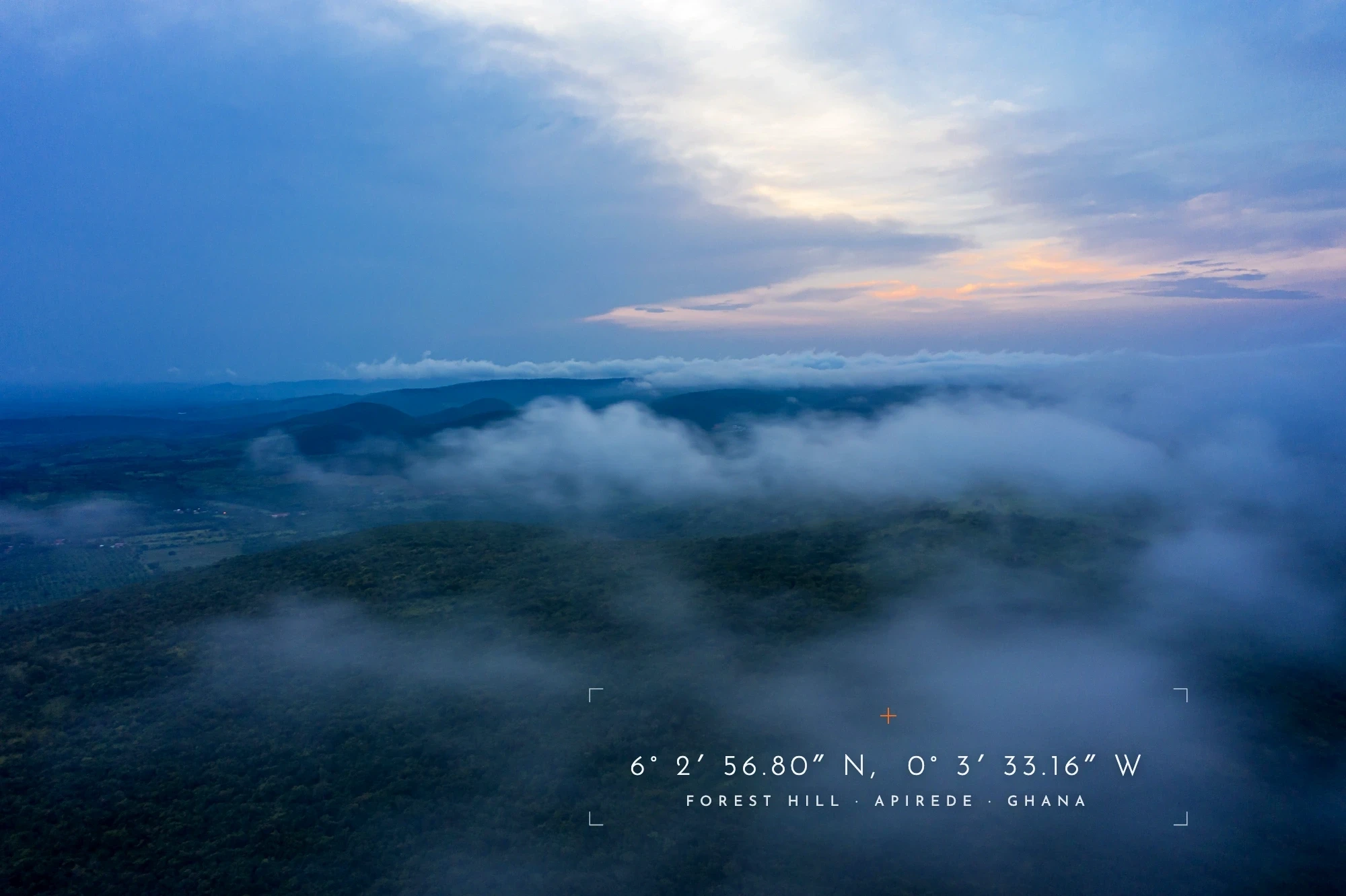 Aerial dusk view above cloud layers over the Akuapem Hills, with distant town lights visible below