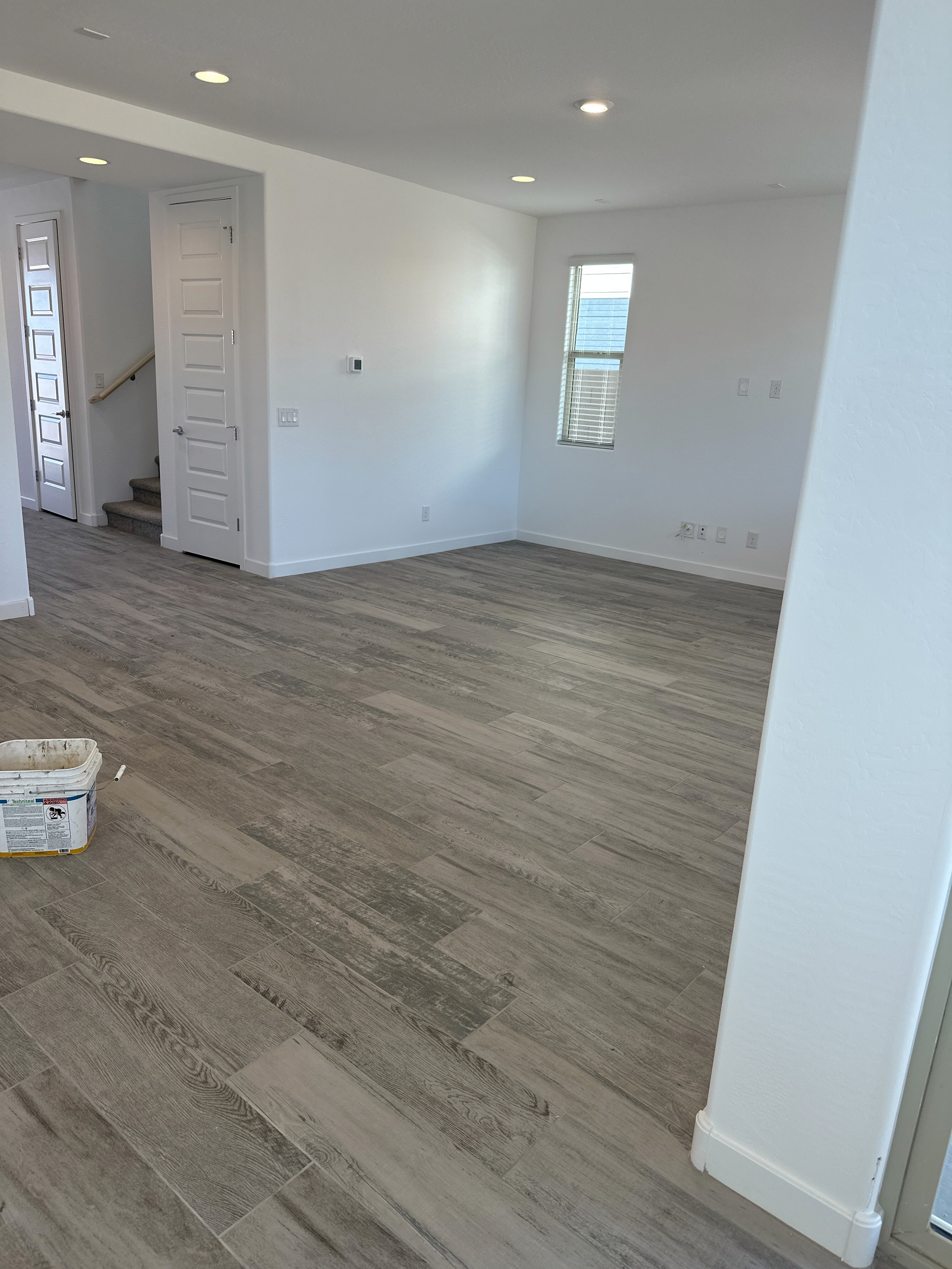 Modern bedroom with wood-look flooring, white walls, and a staircase, featuring construction materials in a new home.