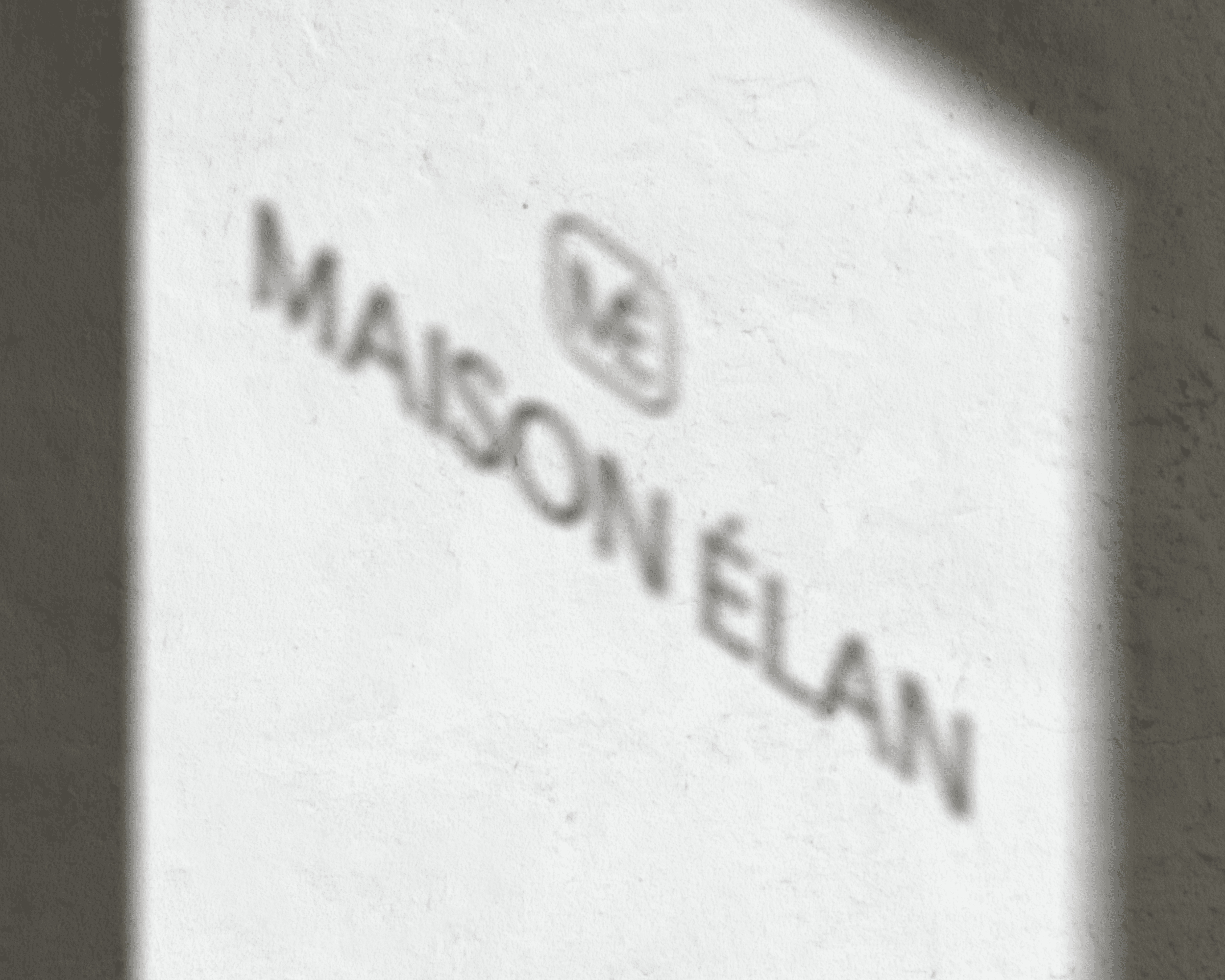 The shadow of the logo design from a storefront window casted on a wall.