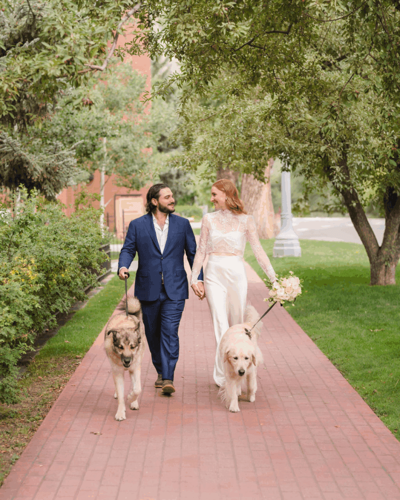 Newlyweds walking two dogs along a garden path