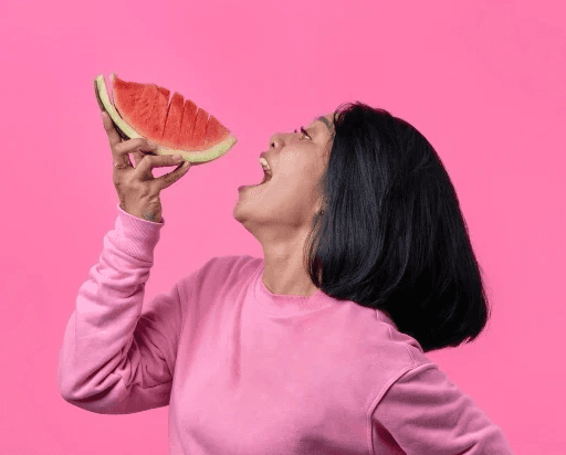 Femme métisse dégustant une tranche de pastèque juteuse, un encas rafraîchissant idéal pour s'hydrater pendant le défi #boosttonmicrobiote.
