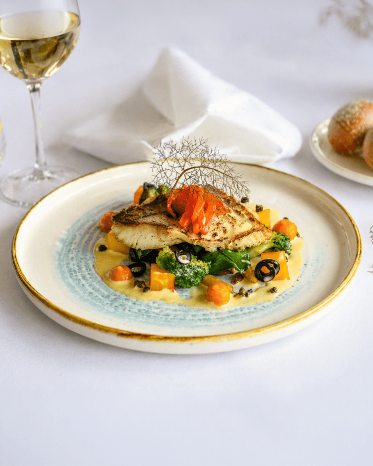 Artfully plated fish dish w/broccoli, orange pieces, black olives, & sauce.