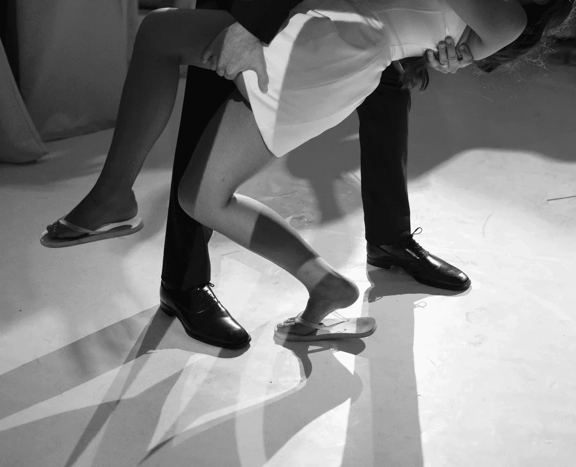 A couple dances closely, showcasing a flowing green dress, against a soft, blurred background of other guests.