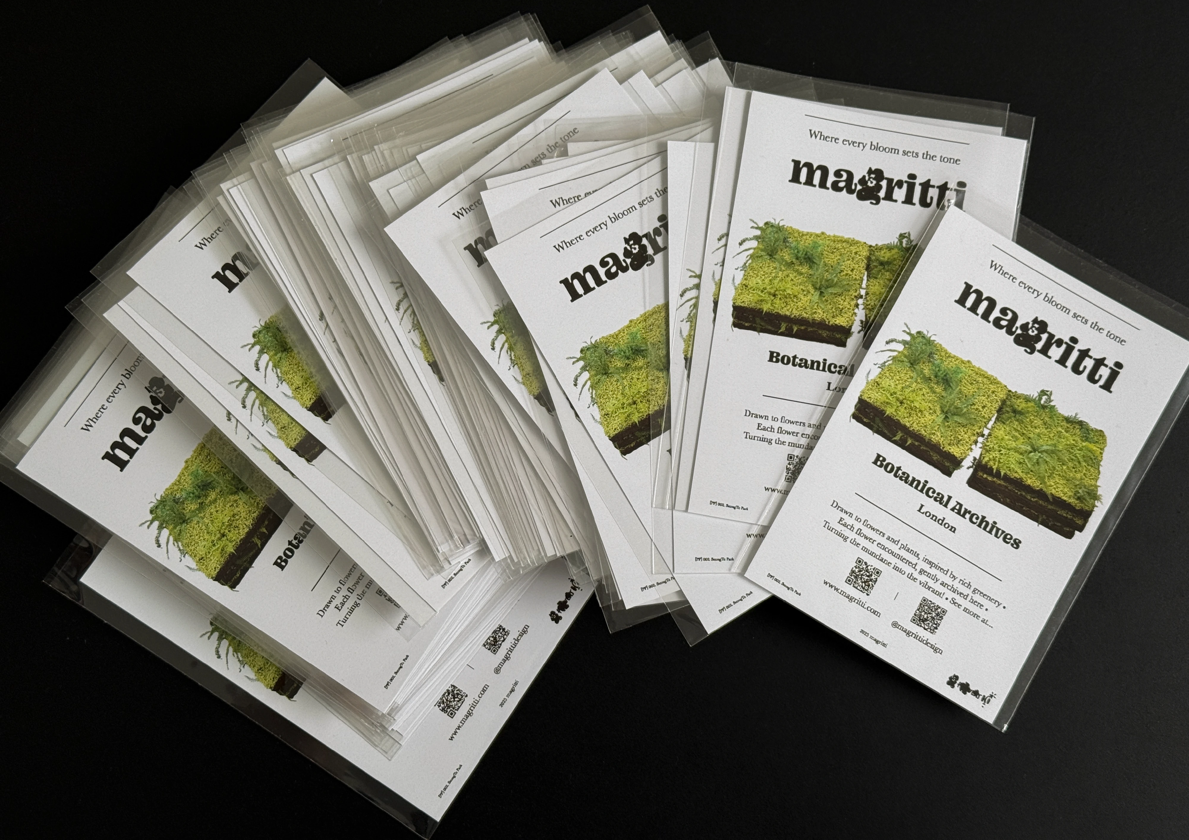A fanned-out pile of sleeved postcards on black, each printed with the same moss-and-fern square and a studio wordmark.