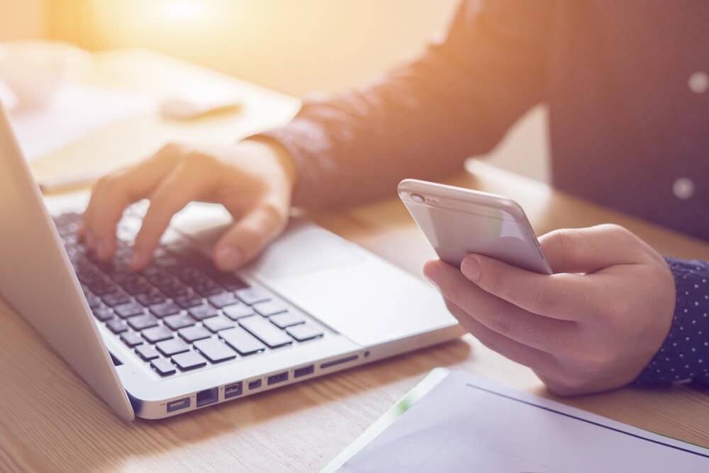 Person using smartphone and laptop at desk