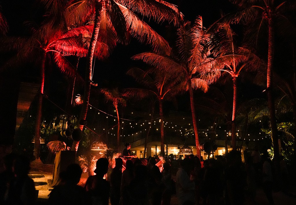 Ambiente festivo en la playa con luces de colores y palmeras de fondo.