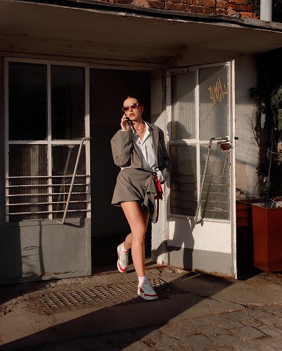 Fotografia lifestyle / modowa, przedstawiająca modelkę rozmawiającą przez telefon, która wychodzi z budynku.