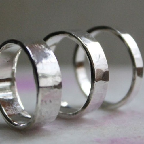 Three silver rings with a hammered texture are aligned in a row against a light-colored background.