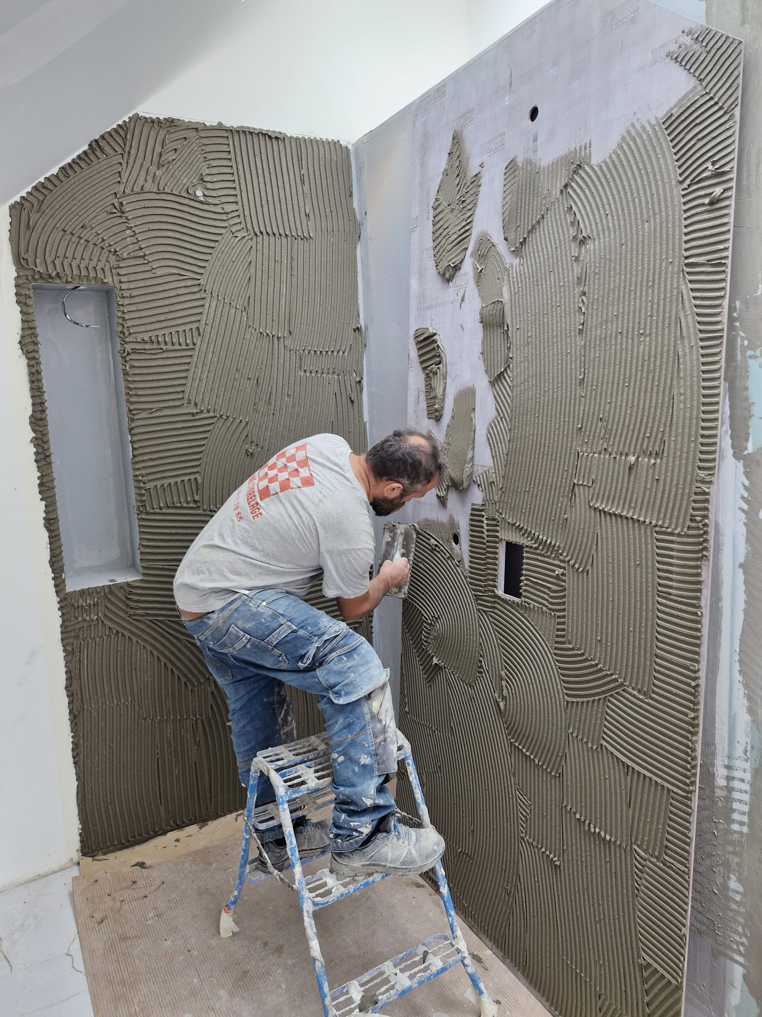 Carreleur appliquant la colle au peigne sur un mur de salle de bain avant la pose de la faïence