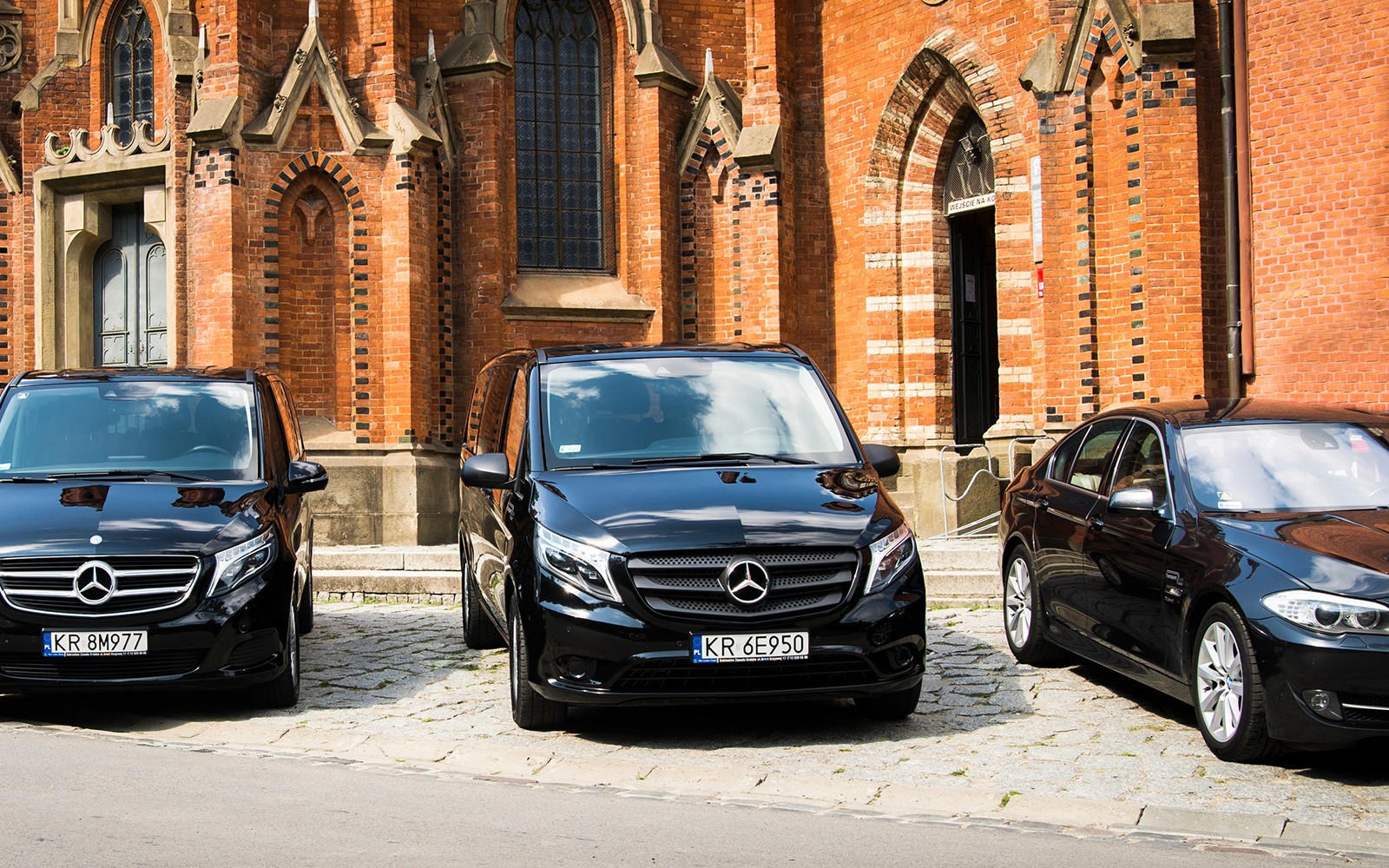 Veicoli Mercedes neri parcheggiati davanti a un edificio storico di mattoni a Cracovia per il transfer all'Aeroporto di Balice.