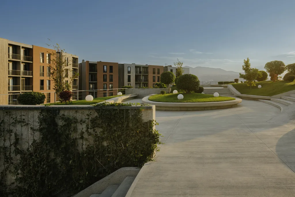 A modern building with greenery, pathways, and mountains in the background under a clear blue sky.