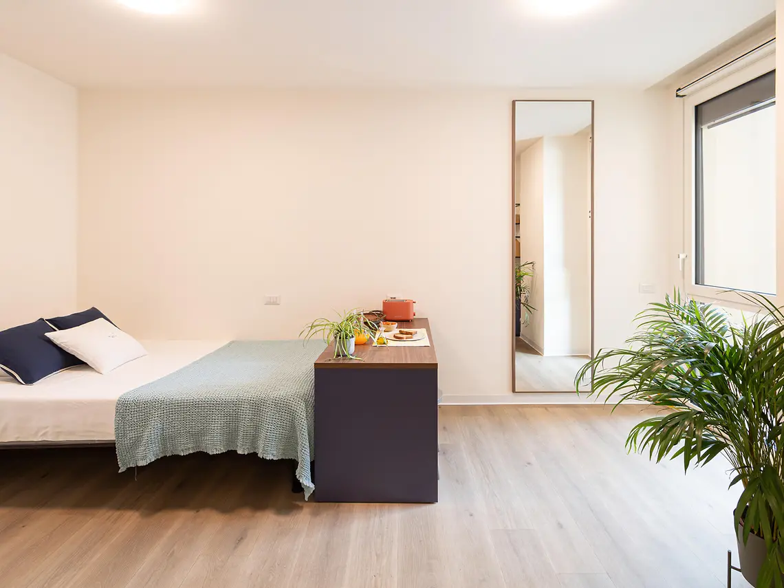 Private student studio bedroom with double bed, throw and full-length mirror — student accommodation in Bologna