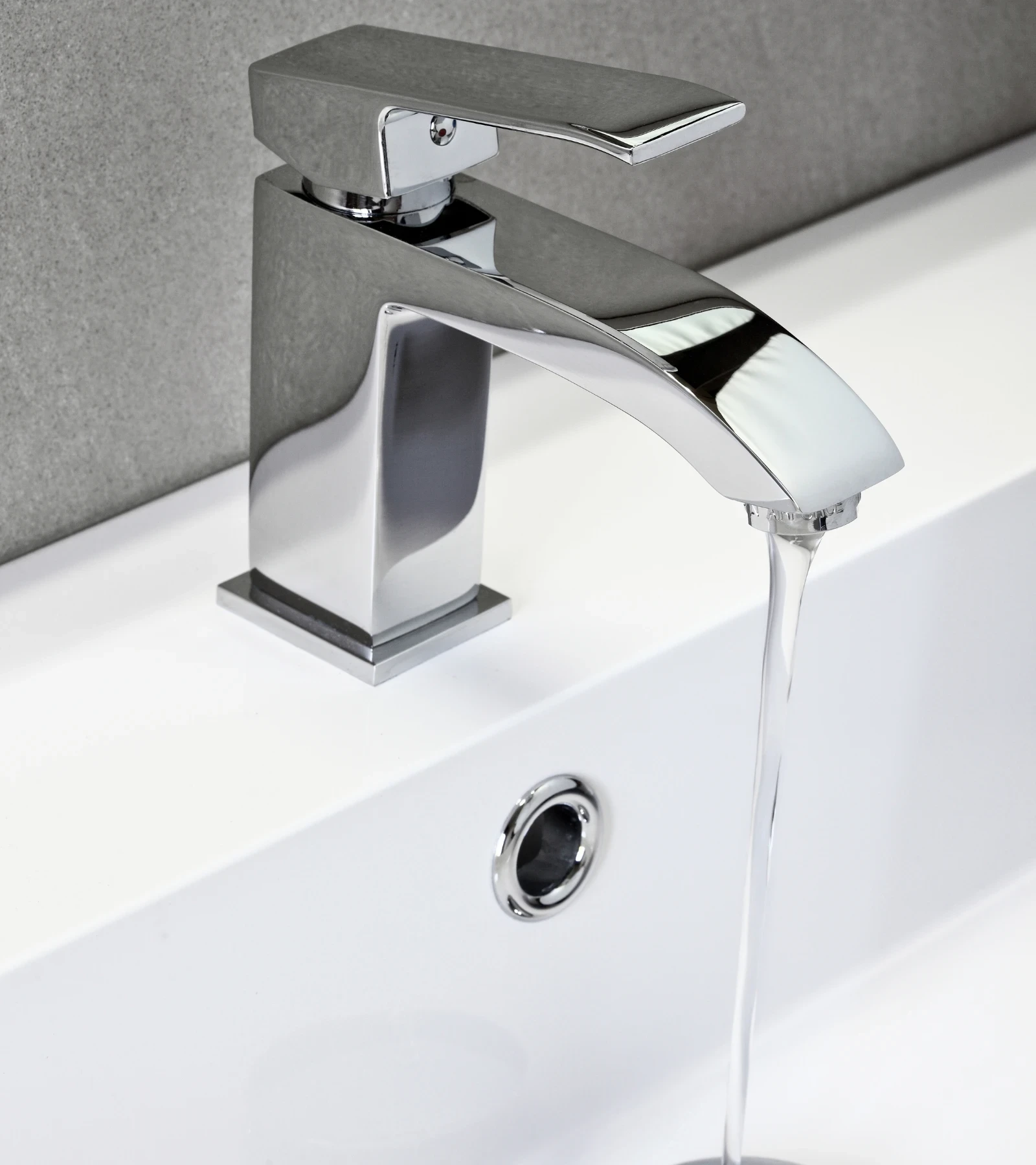 Modern chrome bathroom mixer tap running water into a white basin