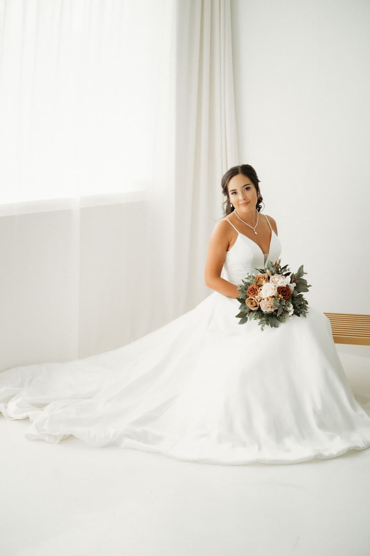 A bride seated in her wedding dress, holding a bouquet of roses and greenery, photographed at Revelator Studio in Shreveport during a studio bridal session.