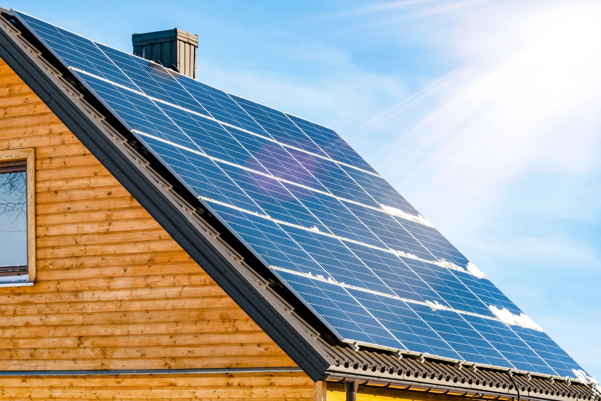 Auf dem Dach eines Holzhauses installierte Solarpaneele unter einem strahlend blauen Himmel.
