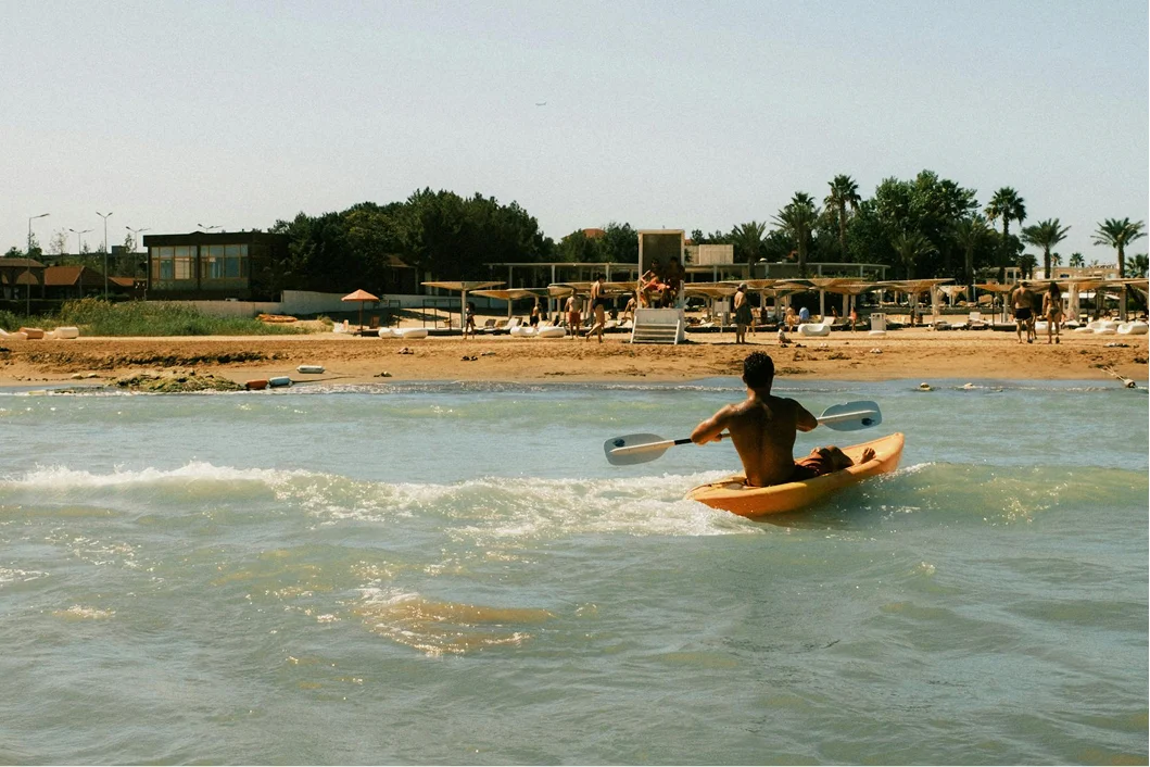 Guest paddling a kayak near the shoreline on a calm beach.