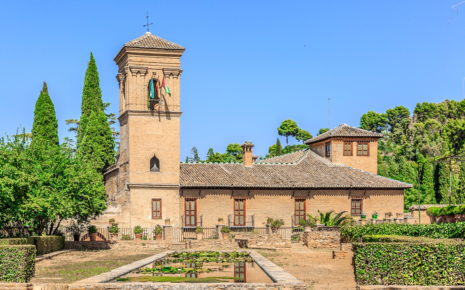 Alhambra-tårnet og hagene med frodig grønt under en klar blå himmel.