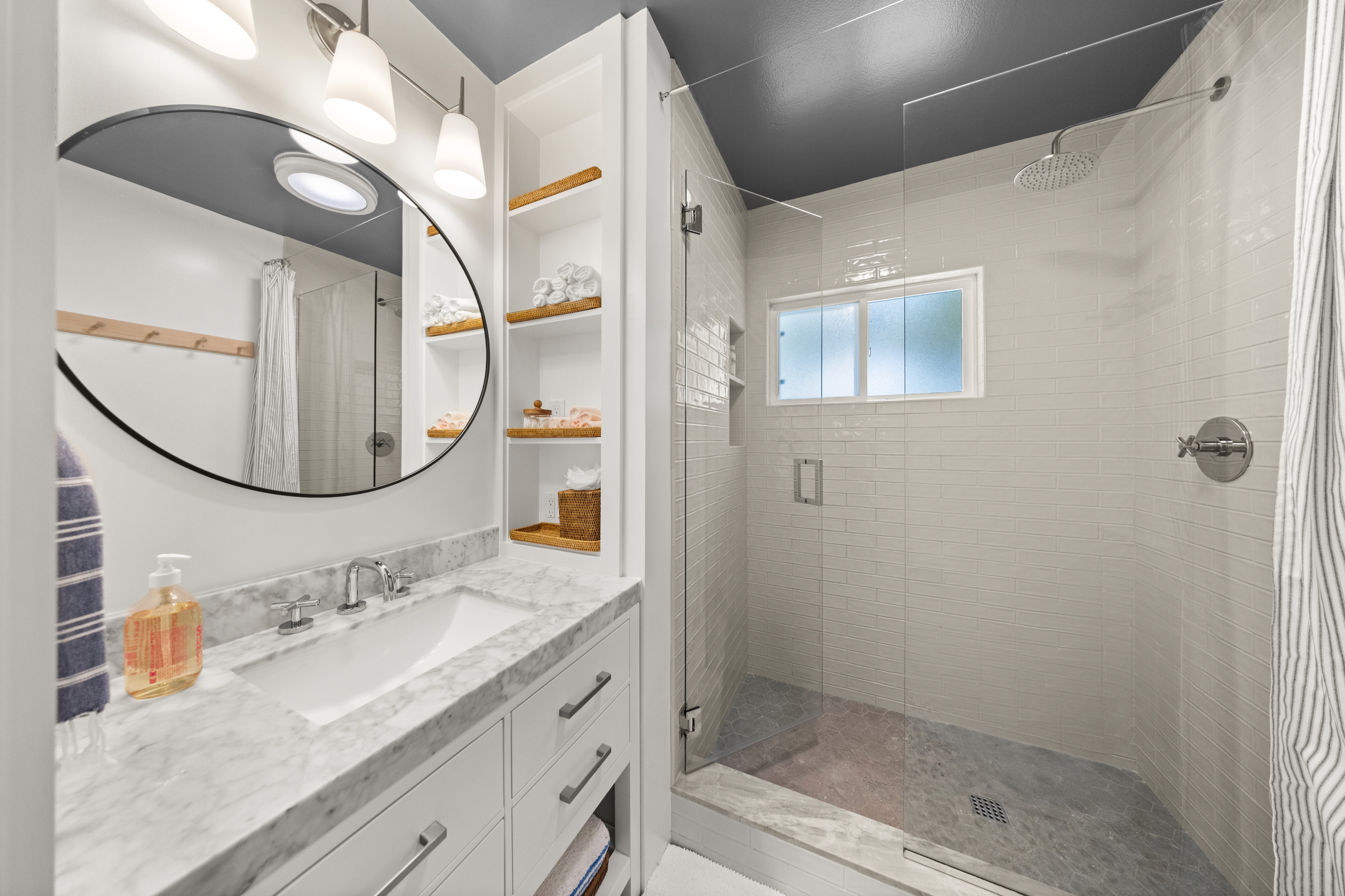 Elegant bathroom with marble countertops, built-in shelving, and a spacious glass-enclosed shower.