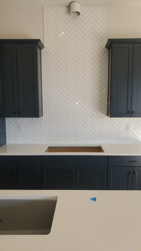 Contemporary kitchen with dark cabinets, a white herringbone tile backsplash, and a sink on a white countertop.