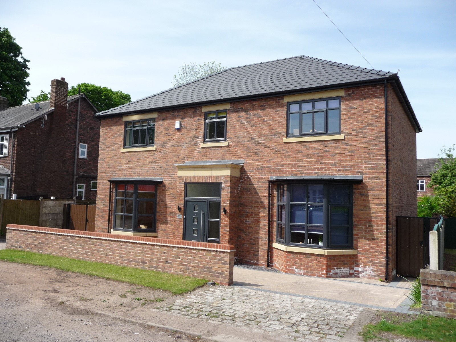 Front elevation of a newly built detached home showing symmetrical bay windows, brickwork, and modern entrance detailing.