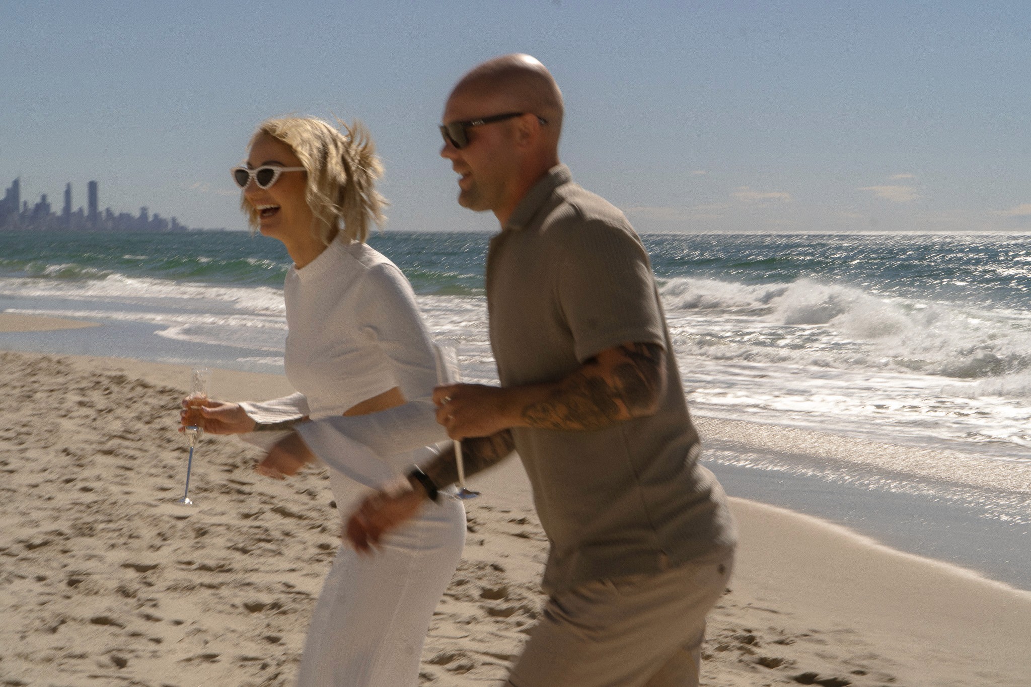Couple walking together beside the surf, with a city skyline in the distance.