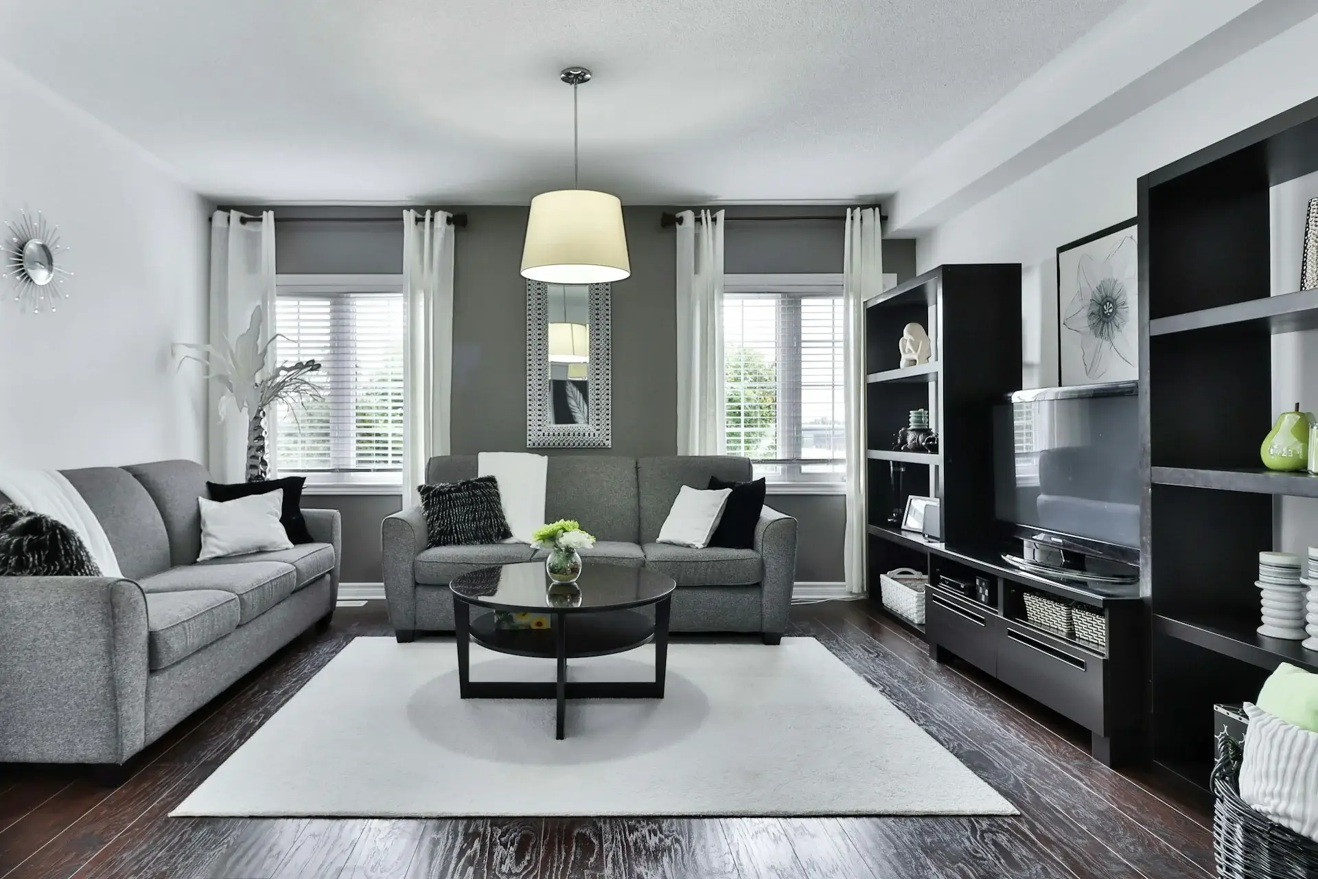 Minimal gray living room with sofas, round table, TV unit, and natural light.