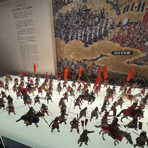 一场展示历史战役艺术作品的活动,其中用红旗、前方的微型士兵战争队形和日文描述文本再现了历史。