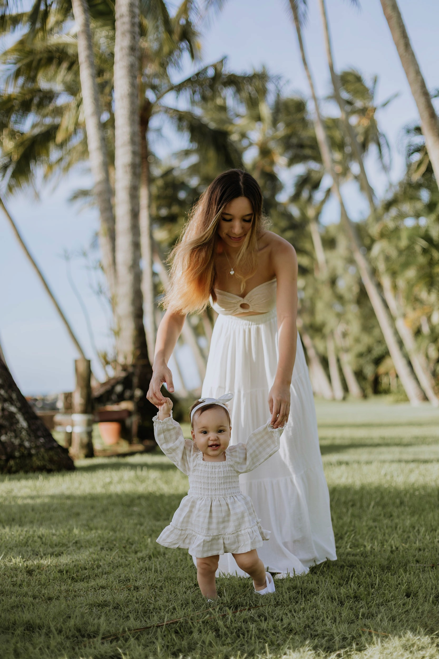Mother and daughter walking together near palm trees during a relaxed outdoor motherhood photography session
