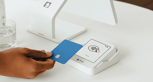 Een hand die een blauwe kaart vasthoudt, staat op het punt op een wit apparaat op een tafel te worden geplaatst.