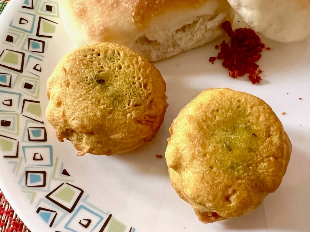 Two batata vadas with 2 pav and spicy garlic coconut chutney is served on a plate