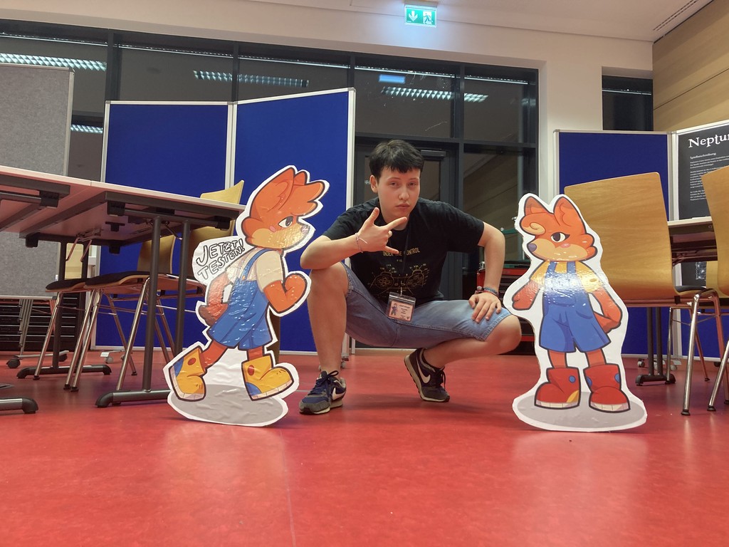 Josef Killinger posing with cardboard cutouts of Carl and Cari from DDI's serious game Carl und Cari: Trubel in Tierstadt
