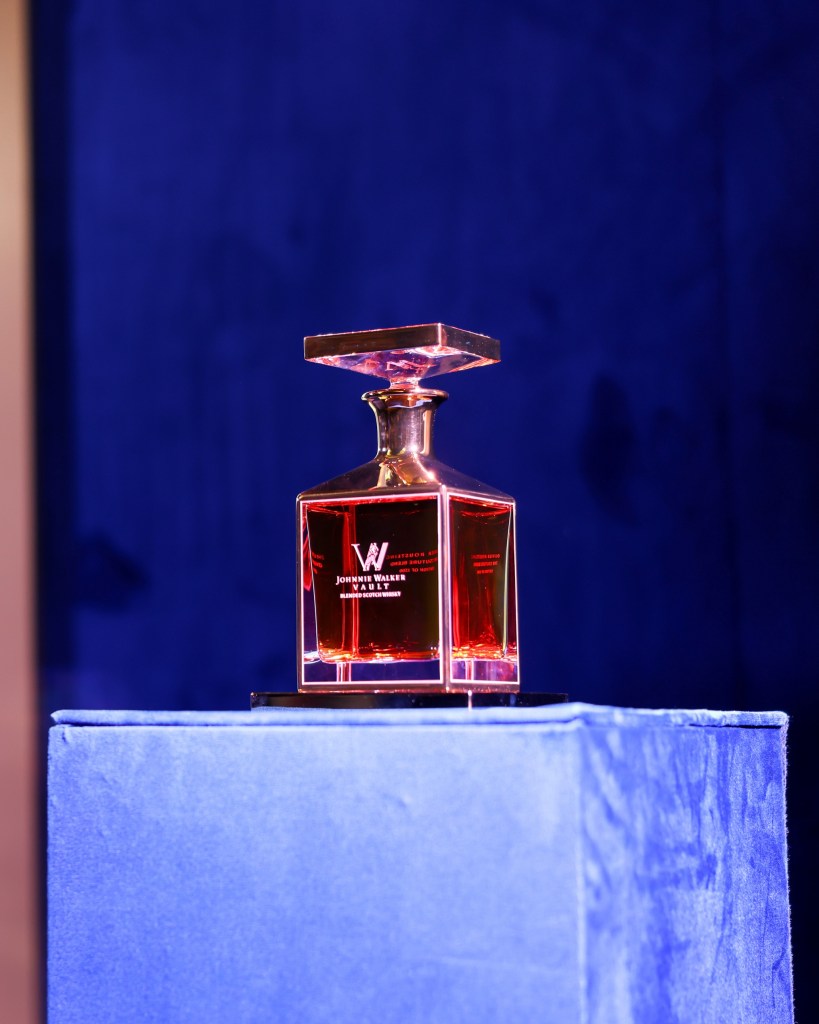 A crystal decanter of Johnnie Walker's Couture Blend whisky, featuring a gold-plated top, displayed on a blue velvet pedestal.