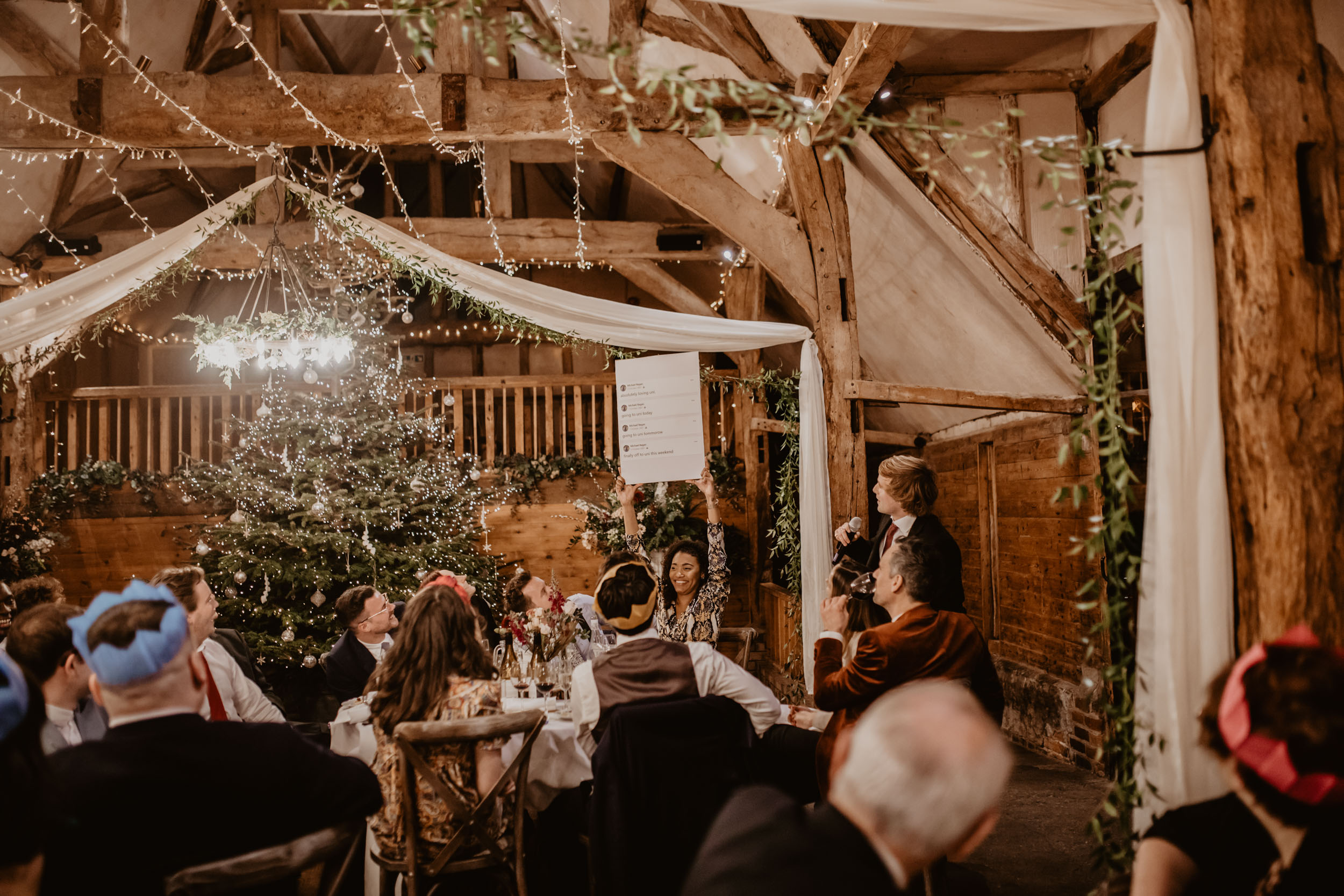 Guest holding card up during speeches in front of the Lains Barn Christmas tree