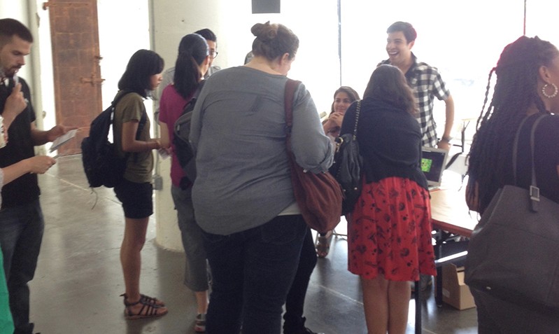 A photo of a group of people sitting around a stand and talking.