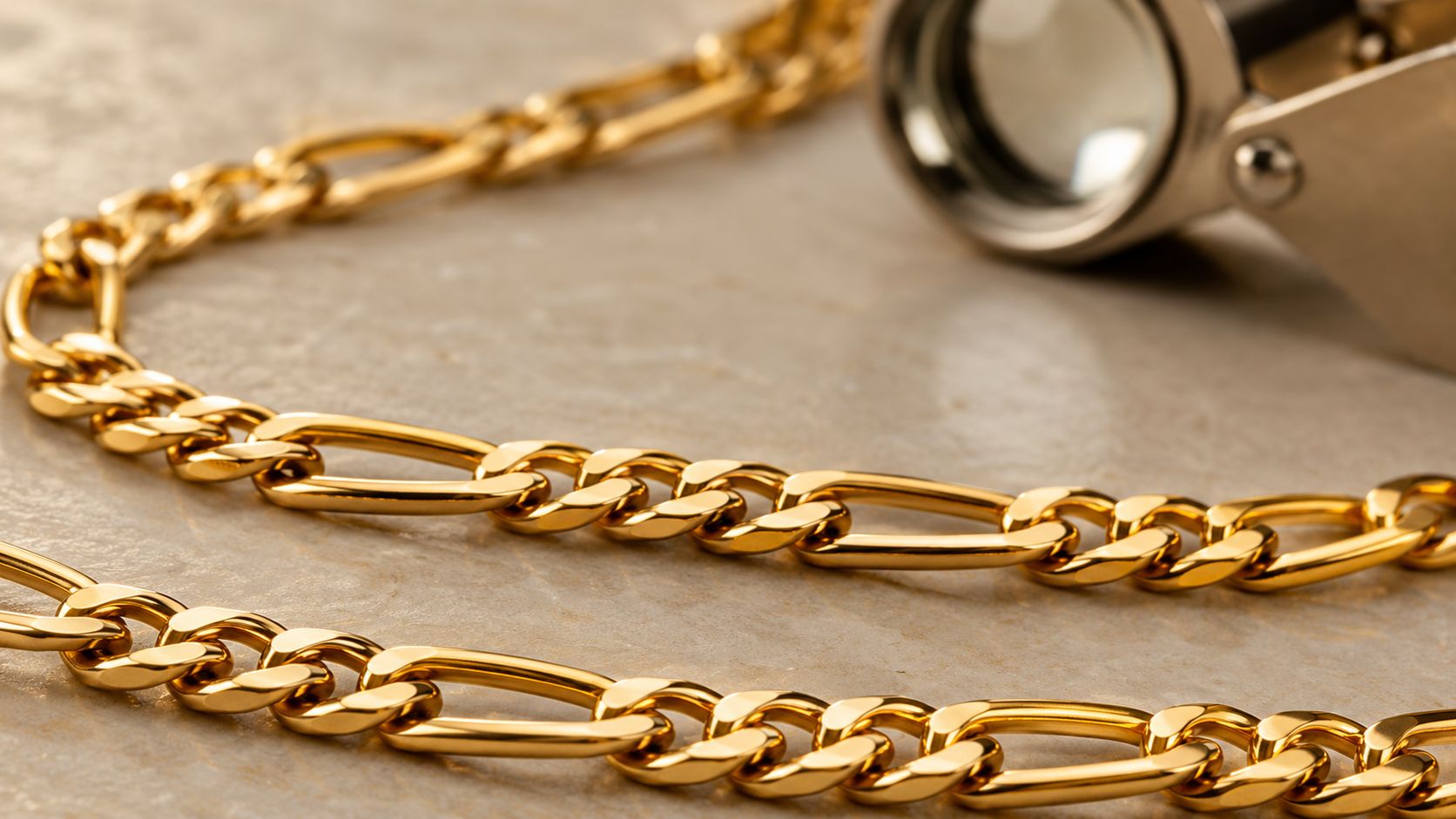 A close-up view of a polished 14k solid gold figaro chain lying on a light textured surface.