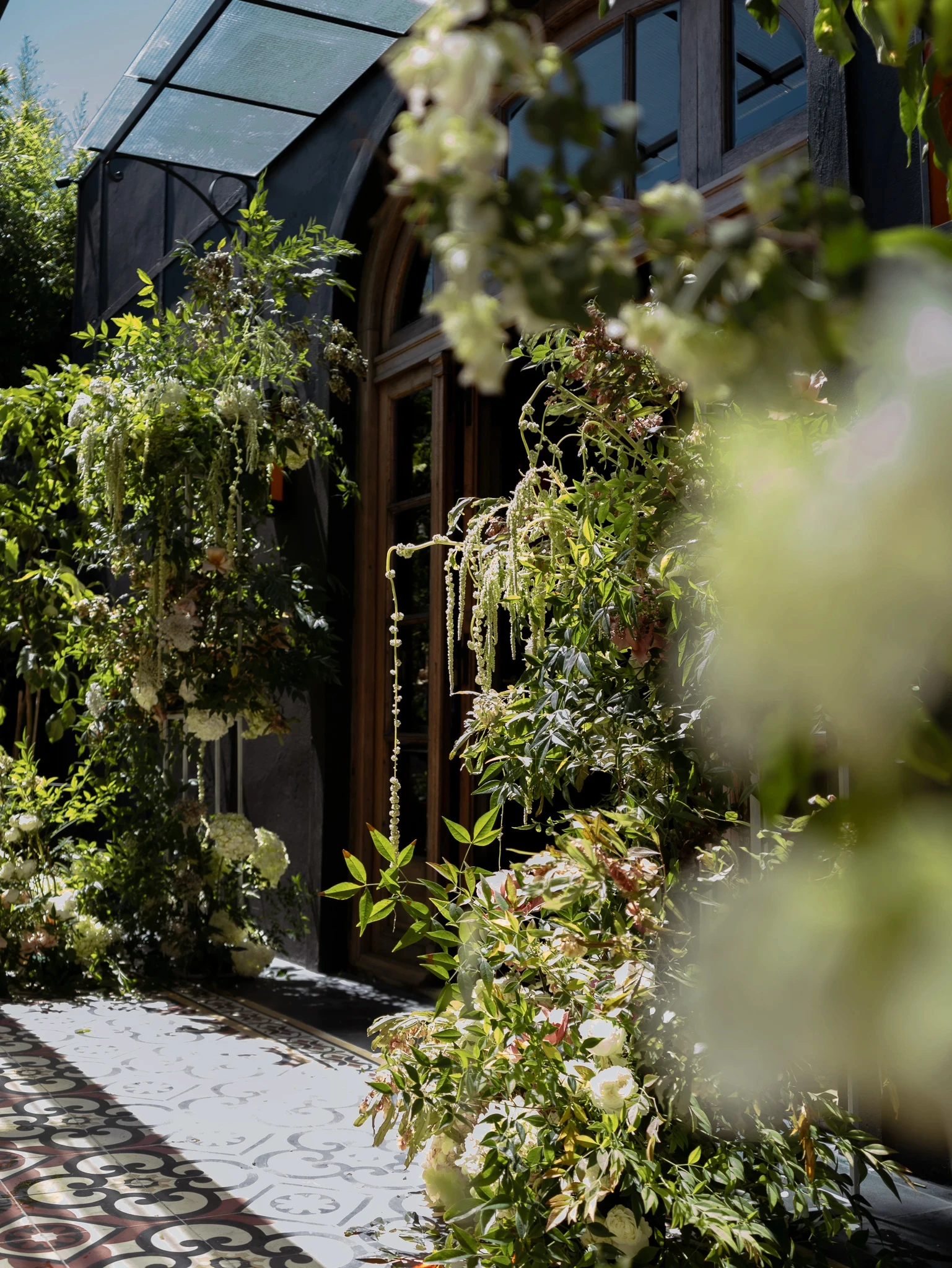 Entrada de Gardiner decorada con flores blancas colgantes y enredaderas naturales sobre piso de mosaicos.