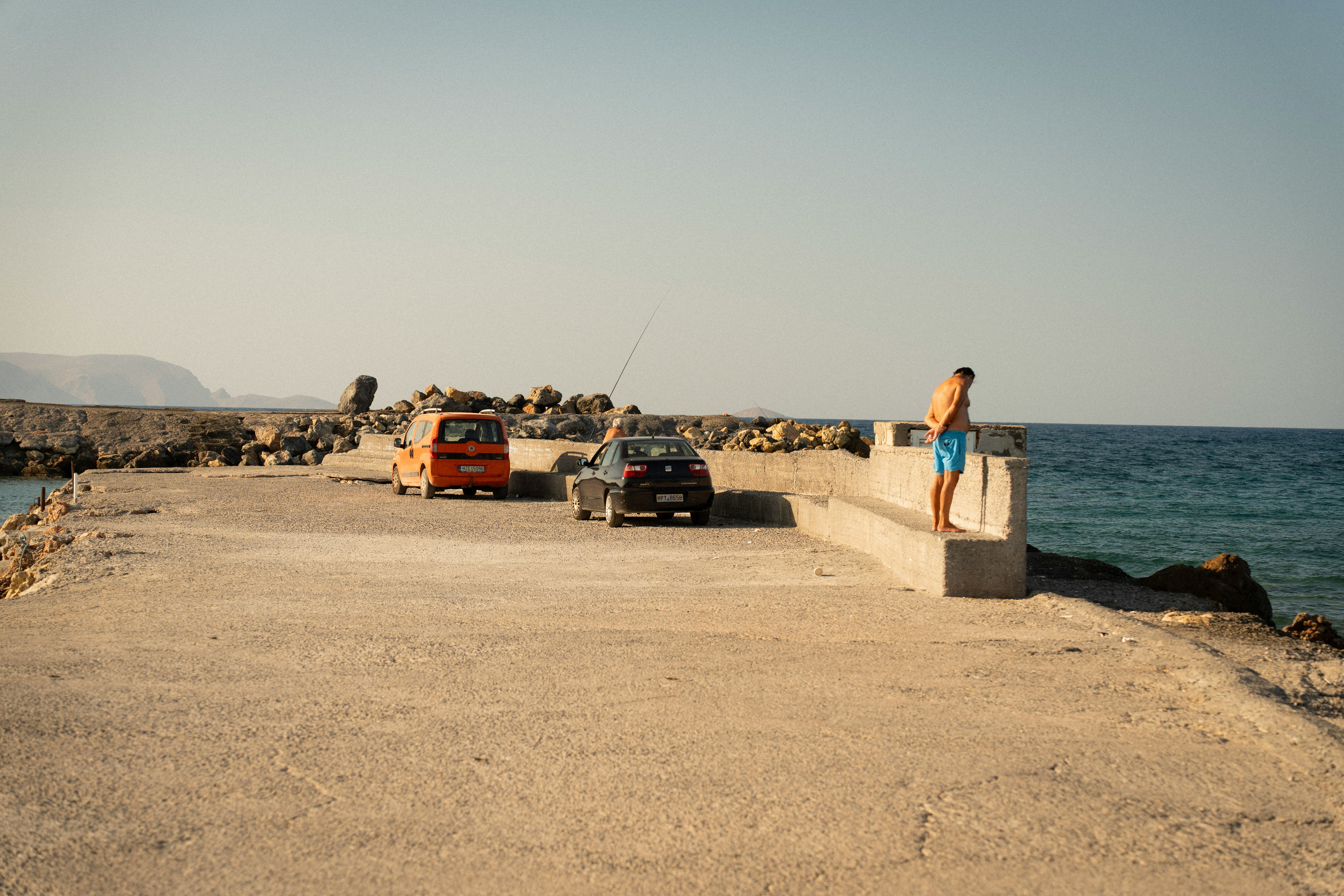 Man on pier overlooking the ocean with two cars.
