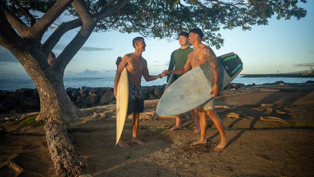 3 surfers greet each other outdoor near beach in Hawai'i