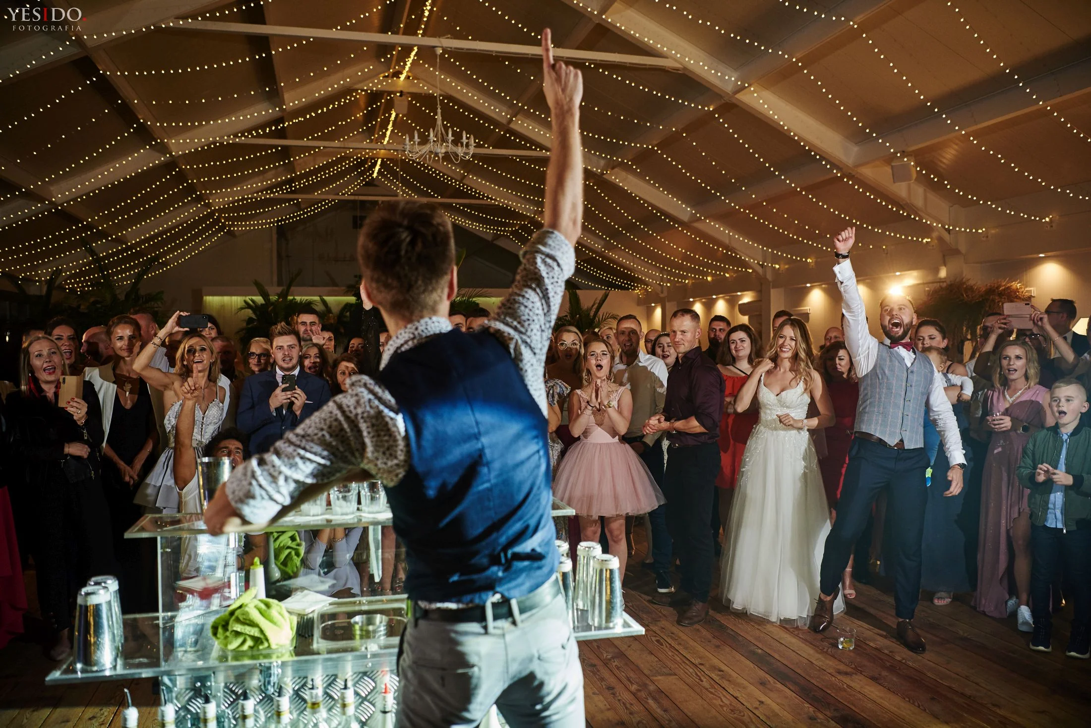 Barman na weselu pokazuje sztuczki barmańskie przed zgromadzonymi gośćmi.