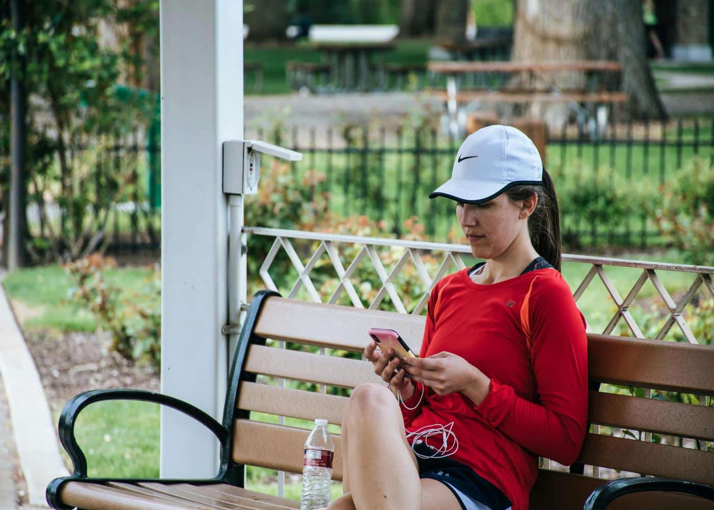 Woman sitting on bench outdoors with workout clothes on looking at smartphone