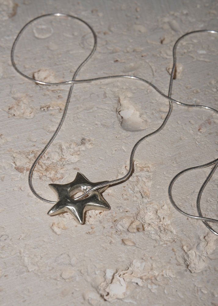 Silver star-shaped pendant on a chain against a textured beige background